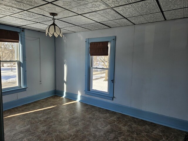 empty room with a drop ceiling, wooden walls, and light hardwood / wood-style floors