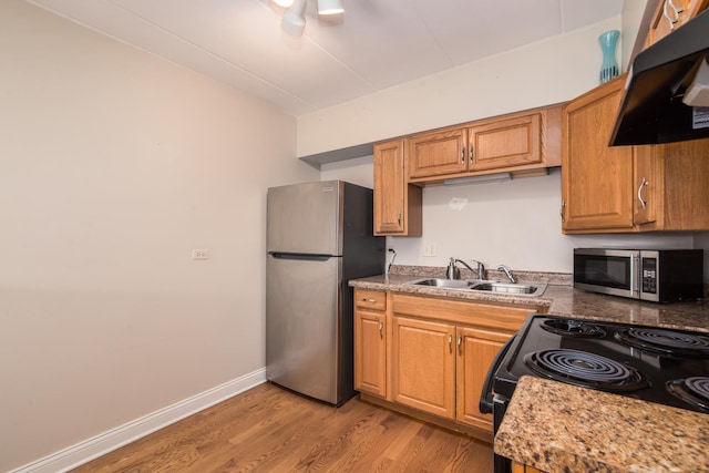 kitchen with light stone counters, extractor fan, light hardwood / wood-style flooring, stainless steel appliances, and sink