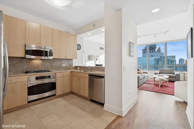 kitchen with sink, tasteful backsplash, light brown cabinetry, rail lighting, and appliances with stainless steel finishes