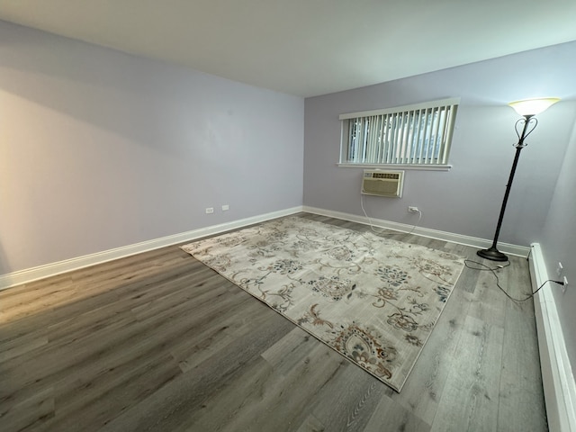 spare room featuring a wall unit AC, baseboards, and wood finished floors