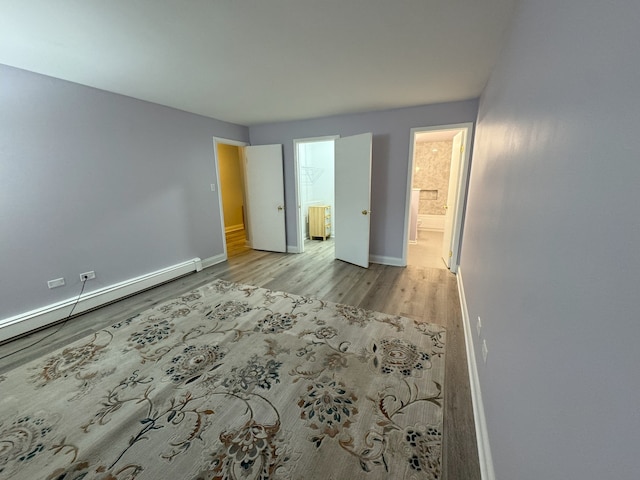 unfurnished bedroom featuring baseboards, a baseboard heating unit, connected bathroom, and light wood-style floors