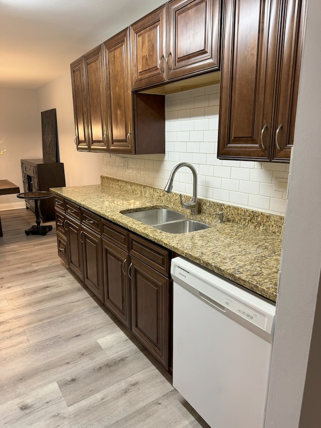 kitchen with light wood-style flooring, light stone counters, a sink, white dishwasher, and backsplash