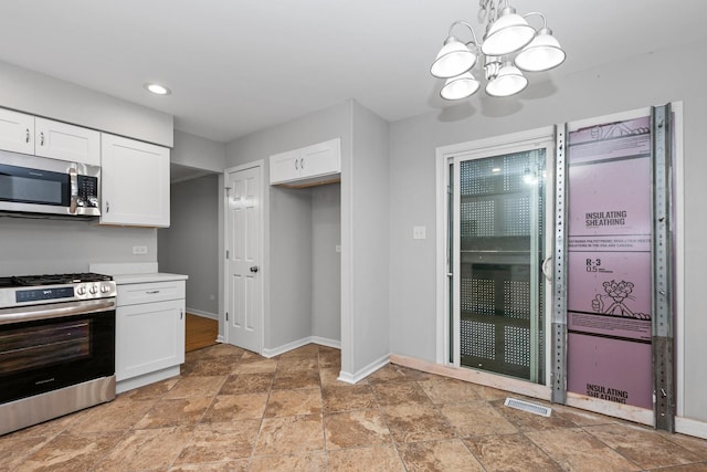 kitchen with appliances with stainless steel finishes, hanging light fixtures, white cabinetry, and an inviting chandelier