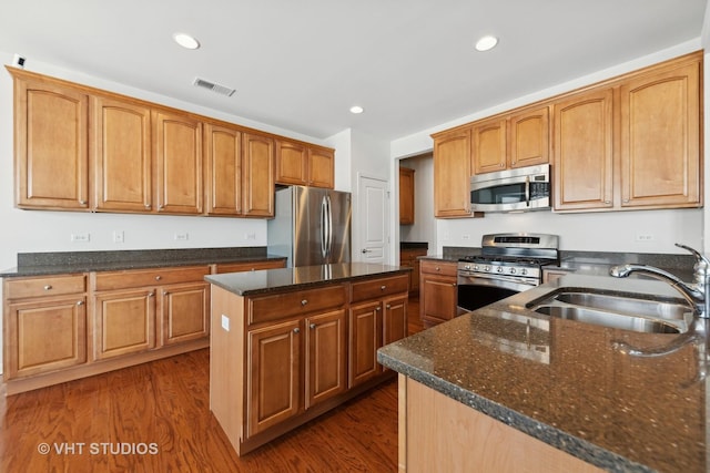 kitchen with sink, appliances with stainless steel finishes, dark hardwood / wood-style floors, a kitchen island, and dark stone counters