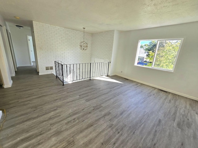 empty room with dark hardwood / wood-style floors, a textured ceiling, and brick wall