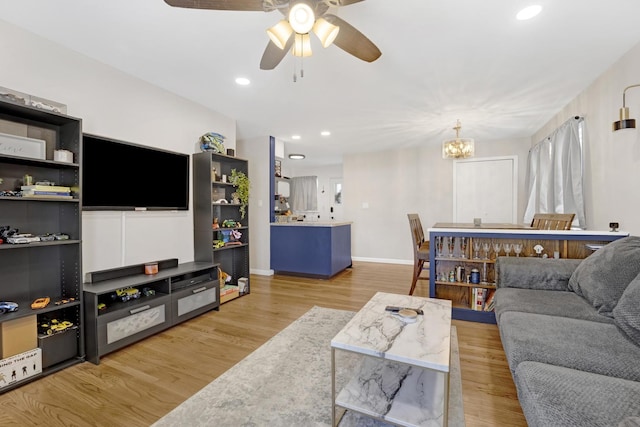 living room featuring ceiling fan with notable chandelier and light hardwood / wood-style flooring