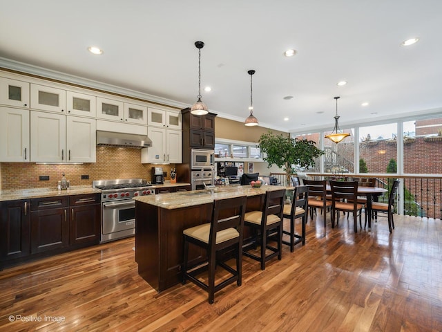 kitchen featuring extractor fan, decorative light fixtures, stainless steel appliances, an island with sink, and light stone counters