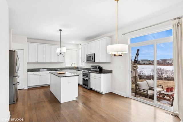 kitchen with decorative light fixtures, dark hardwood / wood-style floors, a kitchen island, appliances with stainless steel finishes, and white cabinets