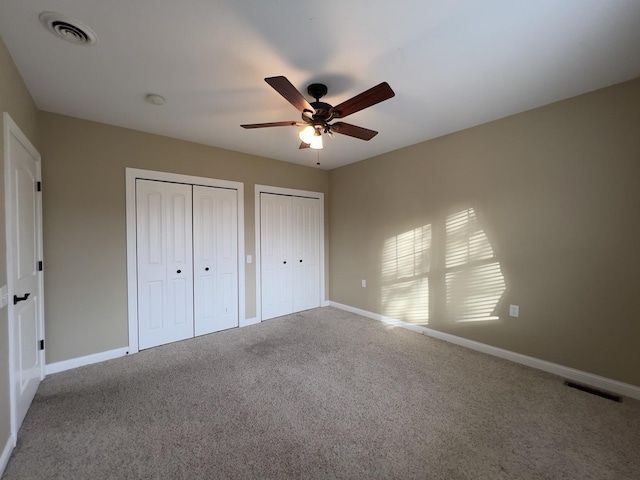 unfurnished bedroom with ceiling fan, carpet flooring, and multiple closets