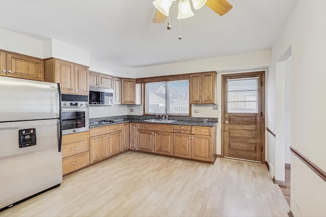 kitchen featuring appliances with stainless steel finishes, sink, dark stone counters, ceiling fan, and light wood-type flooring