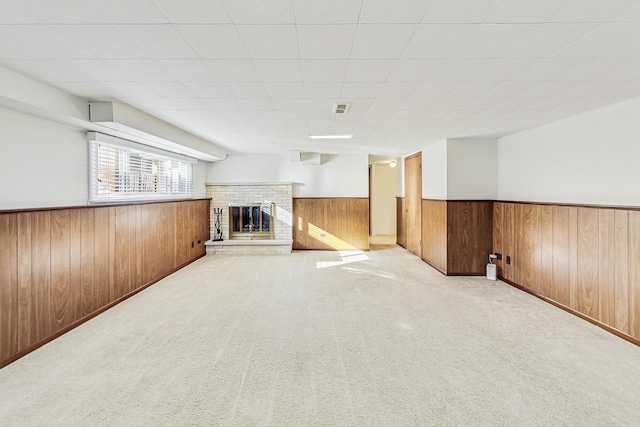 basement with light carpet, a brick fireplace, and wood walls