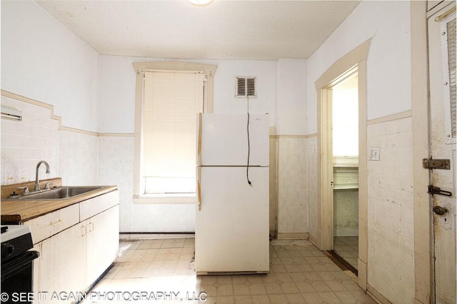 kitchen with visible vents, stove, freestanding refrigerator, wainscoting, and a sink