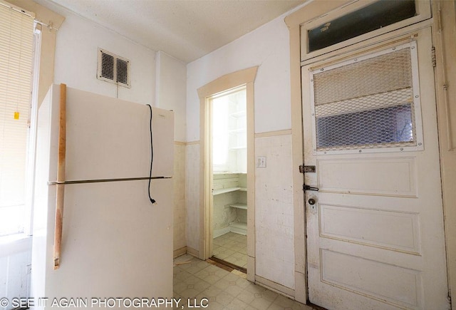 interior space featuring visible vents, tile walls, wainscoting, freestanding refrigerator, and light floors