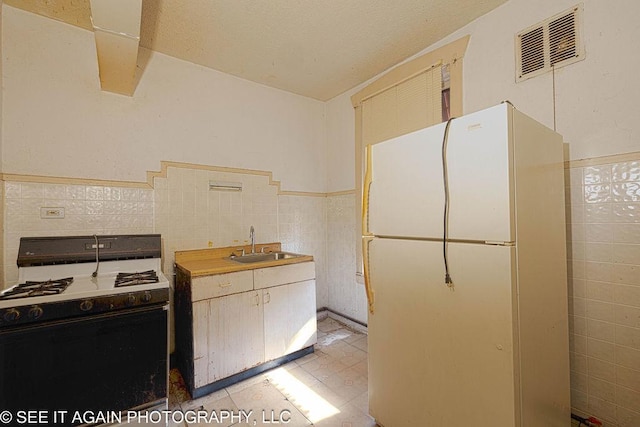 kitchen with visible vents, freestanding refrigerator, a sink, tile walls, and gas stove