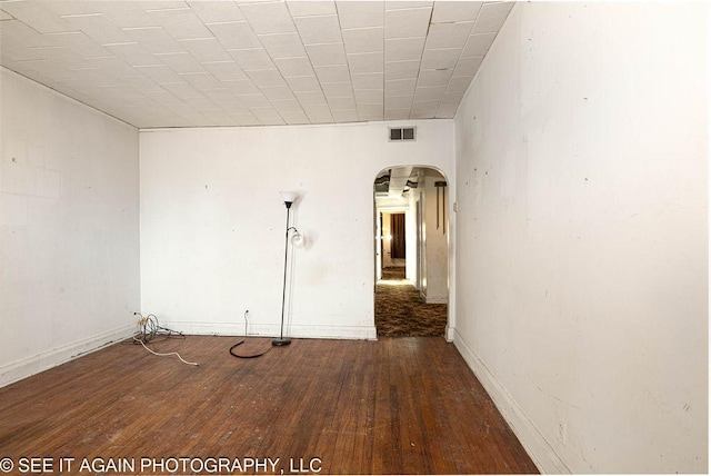 empty room featuring arched walkways, wood-type flooring, visible vents, and baseboards