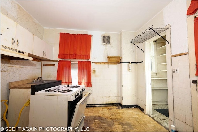 kitchen featuring white cabinetry, white gas range, visible vents, and under cabinet range hood