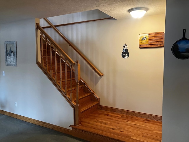 stairs with a textured ceiling and wood-type flooring