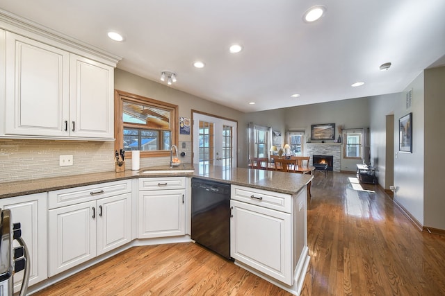 kitchen with sink, dishwasher, white cabinetry, a fireplace, and kitchen peninsula