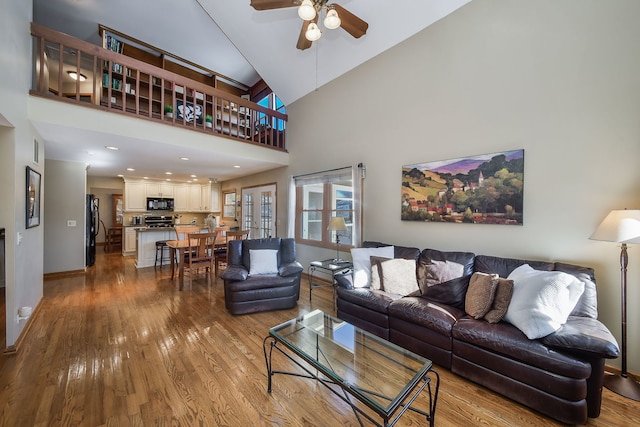 living room with a high ceiling, ceiling fan, and light hardwood / wood-style flooring