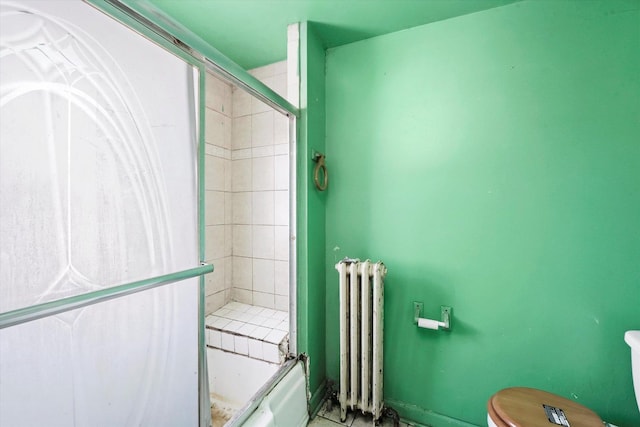 bathroom featuring enclosed tub / shower combo, toilet, and radiator