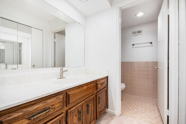 bathroom featuring toilet, vanity, and tile walls