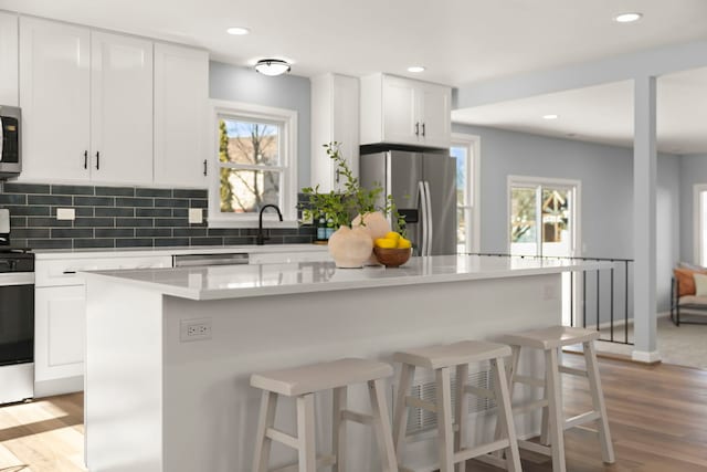 kitchen with stainless steel appliances, a center island, a wealth of natural light, white cabinets, and a kitchen bar