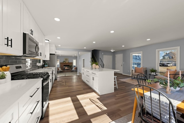 kitchen with stainless steel appliances, a fireplace, white cabinets, dark hardwood / wood-style flooring, and decorative backsplash