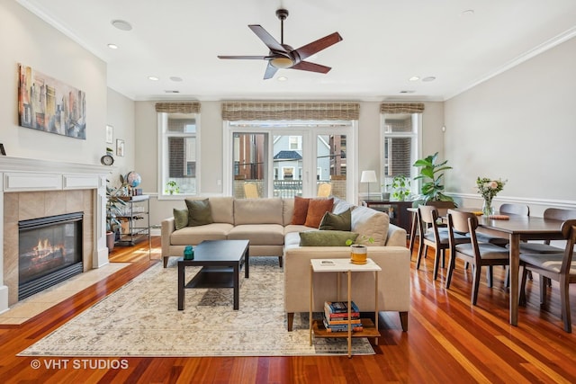 living area with a tiled fireplace, wood finished floors, and crown molding