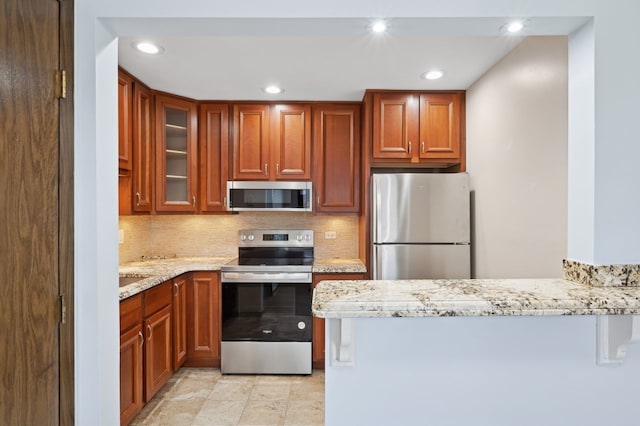 kitchen with appliances with stainless steel finishes, backsplash, kitchen peninsula, and light stone countertops