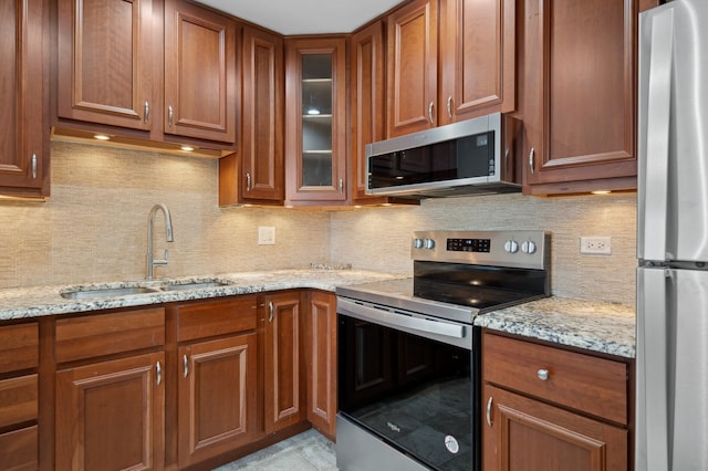 kitchen featuring light stone countertops, backsplash, appliances with stainless steel finishes, and sink