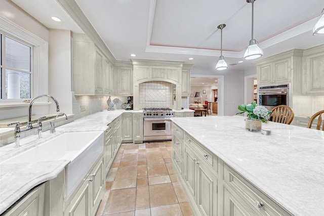 kitchen featuring light stone countertops, tasteful backsplash, pendant lighting, stainless steel appliances, and a tray ceiling