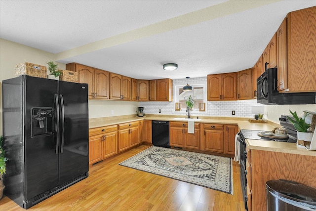 kitchen with tasteful backsplash, sink, black appliances, a textured ceiling, and light hardwood / wood-style flooring