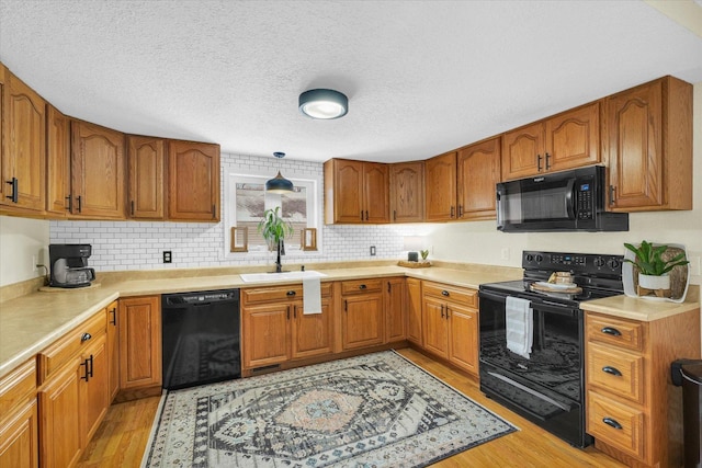 kitchen featuring sink, a textured ceiling, light hardwood / wood-style floors, and black appliances