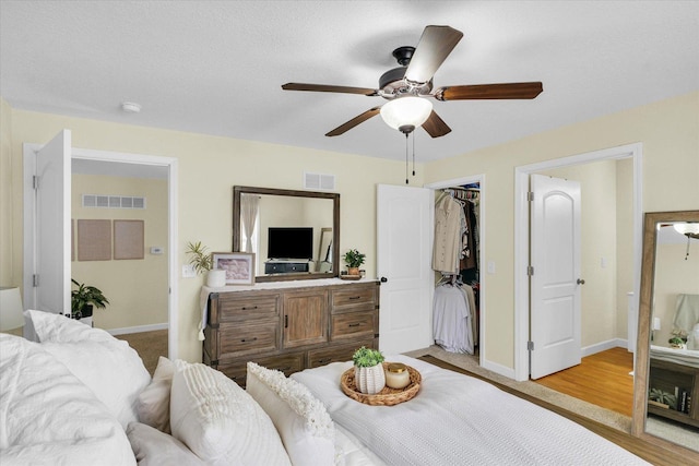 bedroom with light hardwood / wood-style flooring, ceiling fan, a textured ceiling, a walk in closet, and a closet