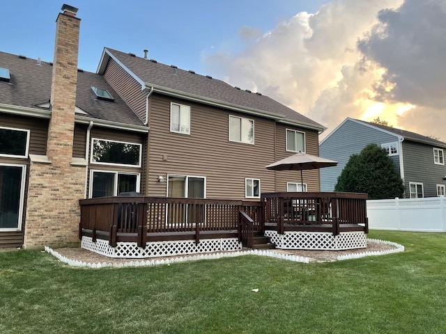 back house at dusk featuring a lawn and a deck