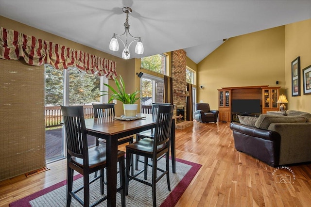 dining space featuring light hardwood / wood-style floors, a brick fireplace, an inviting chandelier, and vaulted ceiling