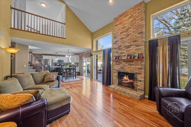 living room with a brick fireplace, high vaulted ceiling, and light hardwood / wood-style flooring