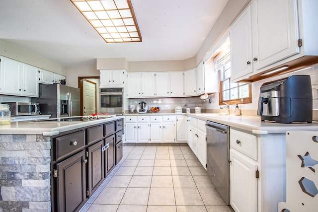 kitchen featuring stainless steel appliances, decorative backsplash, white cabinetry, and light tile patterned floors