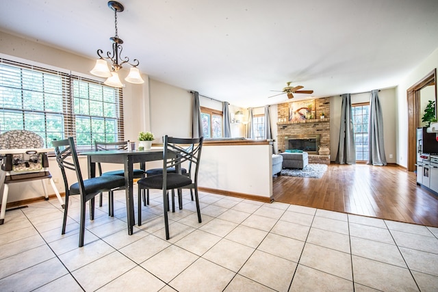 tiled dining space with ceiling fan with notable chandelier, a brick fireplace, and a wealth of natural light