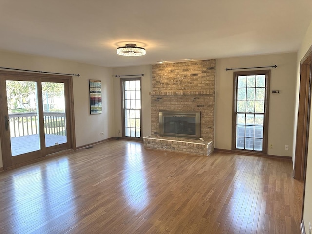 unfurnished living room featuring a brick fireplace, hardwood / wood-style floors, and a healthy amount of sunlight