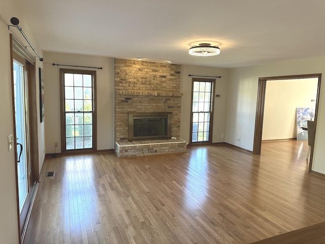 unfurnished living room featuring a brick fireplace, hardwood / wood-style floors, and a healthy amount of sunlight