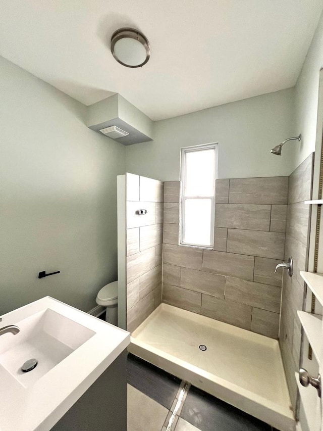 bathroom with toilet, a tile shower, and vanity