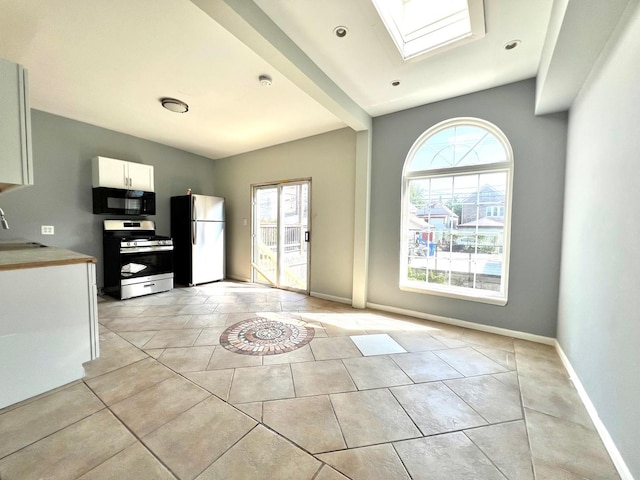 kitchen featuring refrigerator, a skylight, white cabinets, stainless steel range with gas stovetop, and sink