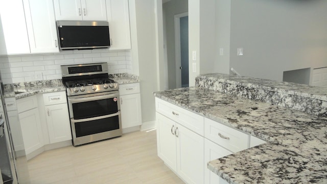 kitchen with double oven range, white cabinets, tasteful backsplash, and light stone countertops