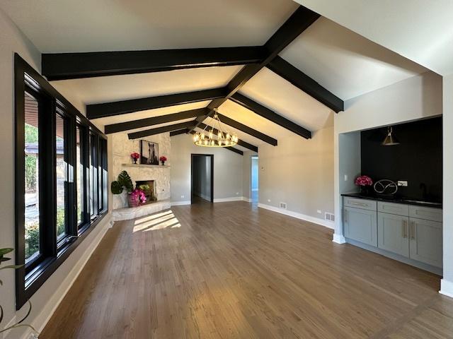 unfurnished living room featuring vaulted ceiling with beams, an inviting chandelier, a fireplace, and dark hardwood / wood-style flooring