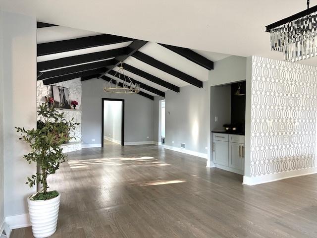 unfurnished living room featuring dark wood-type flooring, an inviting chandelier, and vaulted ceiling with beams