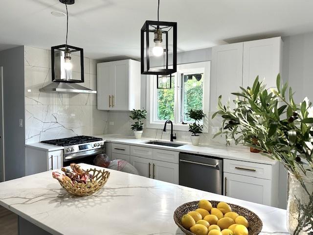 kitchen with light stone countertops, appliances with stainless steel finishes, pendant lighting, and wall chimney range hood