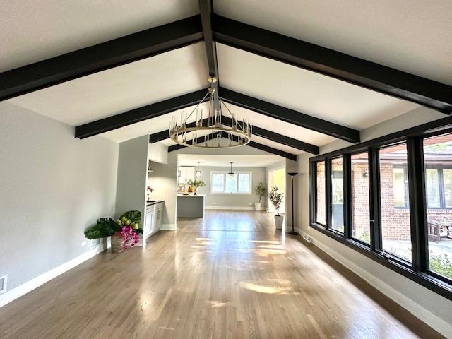 unfurnished living room with a chandelier, hardwood / wood-style floors, and vaulted ceiling with beams