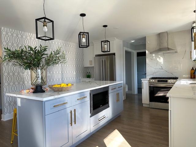 kitchen featuring white cabinetry, appliances with stainless steel finishes, pendant lighting, and wall chimney range hood