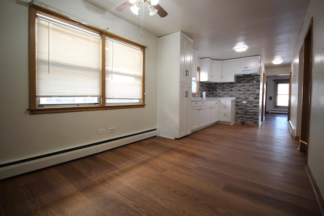 kitchen with white cabinets, ceiling fan, a baseboard heating unit, backsplash, and dark wood-type flooring